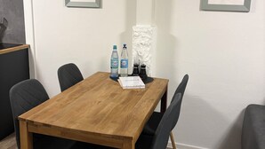 Une table de salle à manger en bois, des chaises noires, deux tableaux encadrés accrochés aux murs et un mur blanc à la texture particulière.
