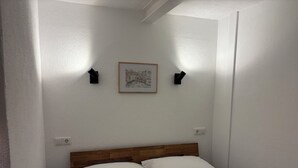 Une chambre à coucher avec une tête de lit en bois, du linge de lit blanc, un tableau encadré au mur et deux appliques murales.