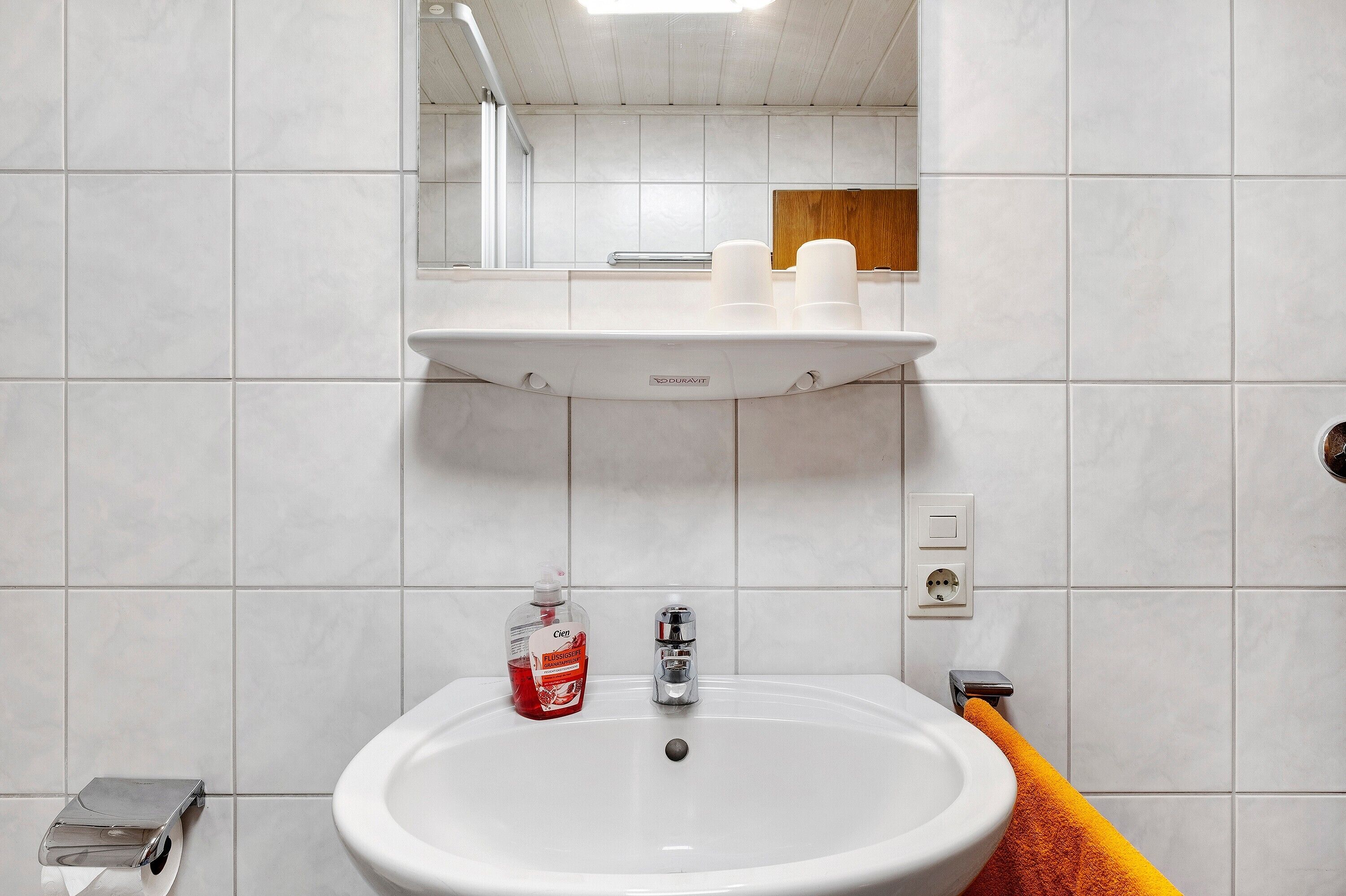 Ein Badezimmer mit weißem Waschbecken, einem Spiegel, einem Handtuchhalter und einer Seifenspender.