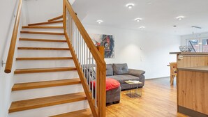 A modern interior with a wooden staircase, a gray sofa, and a wooden dining area.