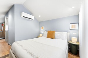 A hotel room with a bed, bedside lamps, a wall-mounted air conditioner, and a framed picture on the wall. - GuestReady - City centre stay in Porto (Porto)