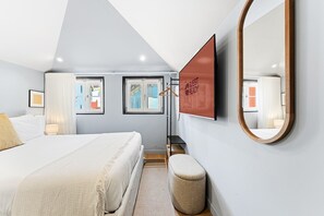 A modern hotel room with a large bed, a flat-screen TV, a mirror, and a view of the city through the windows. - GuestReady - City centre stay in Porto (Porto)