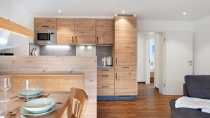A modern kitchen with wooden cabinets, a microwave, and a dining area with a table set for two. - Apartment Wiesenblick with Balcony and Wi-Fi (Horben)