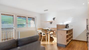 A modern room with a wooden dining table, chairs, a sofa, and a kitchen area with a coffee maker.