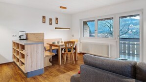 A modern kitchen with a wooden island, a dining table with chairs, and a view through a large window. - Apartment Talblick with Balcony and Wi-Fi (Horben)