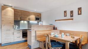 A modern kitchen with wooden cabinetry, a built-in microwave, and a dining area with a bench and chairs. - Apartment Talblick with Balcony and Wi-Fi (Horben)
