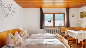 Una habitación con techo de madera, una cama con almohadas coloridas, una mesa con mantel blanco y una ventana con cortinas.