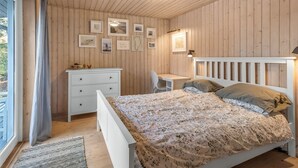 Une chambre avec un plafond en bois, un lit recouvert d’une couvre-lit à motifs floraux, une table de chevet, un bureau et des tableaux encadrés accrochés au mur.