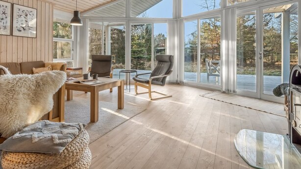 Un vaste salon doté d  ’un plafond en bois, de grandes fenêtres et d’une vue sur une zone boisée.