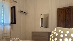 Un dormitorio con cama, lámpara de noche, espejo, equipo de aire acondicionado y armario de madera.