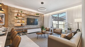 A modern living room with a large TV, comfortable seating, a dining area, and a view of the outdoors.