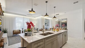 A modern kitchen with a central island, pendant lighting, and a large window.