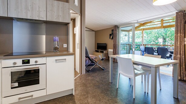 A modern kitchen with built-in appliances, a dining area with a table and chairs, and a large window offering a view of greenery.