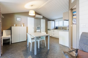 Kompakti keittiö, jossa on ruokapöytä ja -tuolit, pieni jääkaappi ja ikkuna.