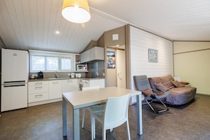 Une cuisine compacte dotée d’appareils électroménagers modernes, un coin repas avec une table et des chaises, et un coin salon confortable avec un fauteuil rembourré.
