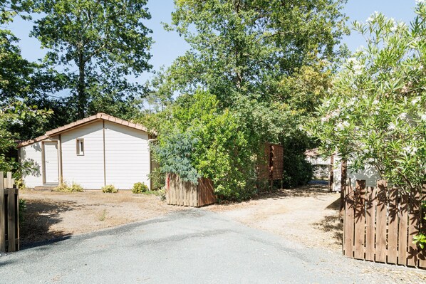 A white single-story house with a gravel driveway, surrounded by trees and a wooden fence.