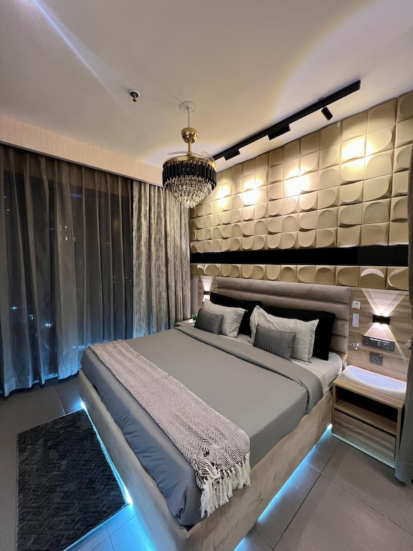 A modern bedroom with a large bed, a chandelier, and a wall-mounted light fixture. - 41 Floor River View - TheRoomeraStay (Noida)