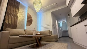 Una sala moderna con un sofá color beige, una mesa de centro de madera y una araña.