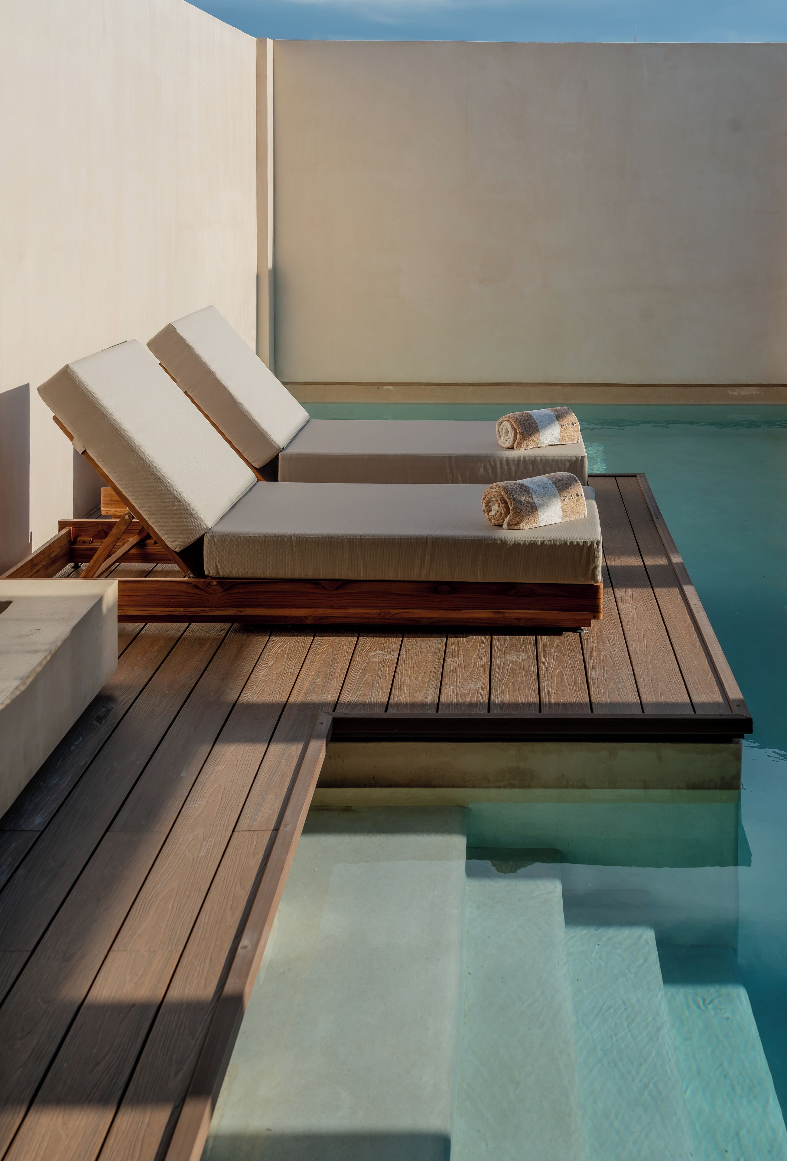 A poolside lounge area with wooden flooring, a couple of lounge chairs, and a small pool.