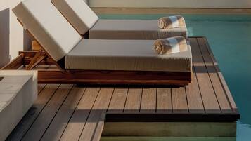 A poolside lounge area with wooden flooring, a couple of lounge chairs, and a small pool.
