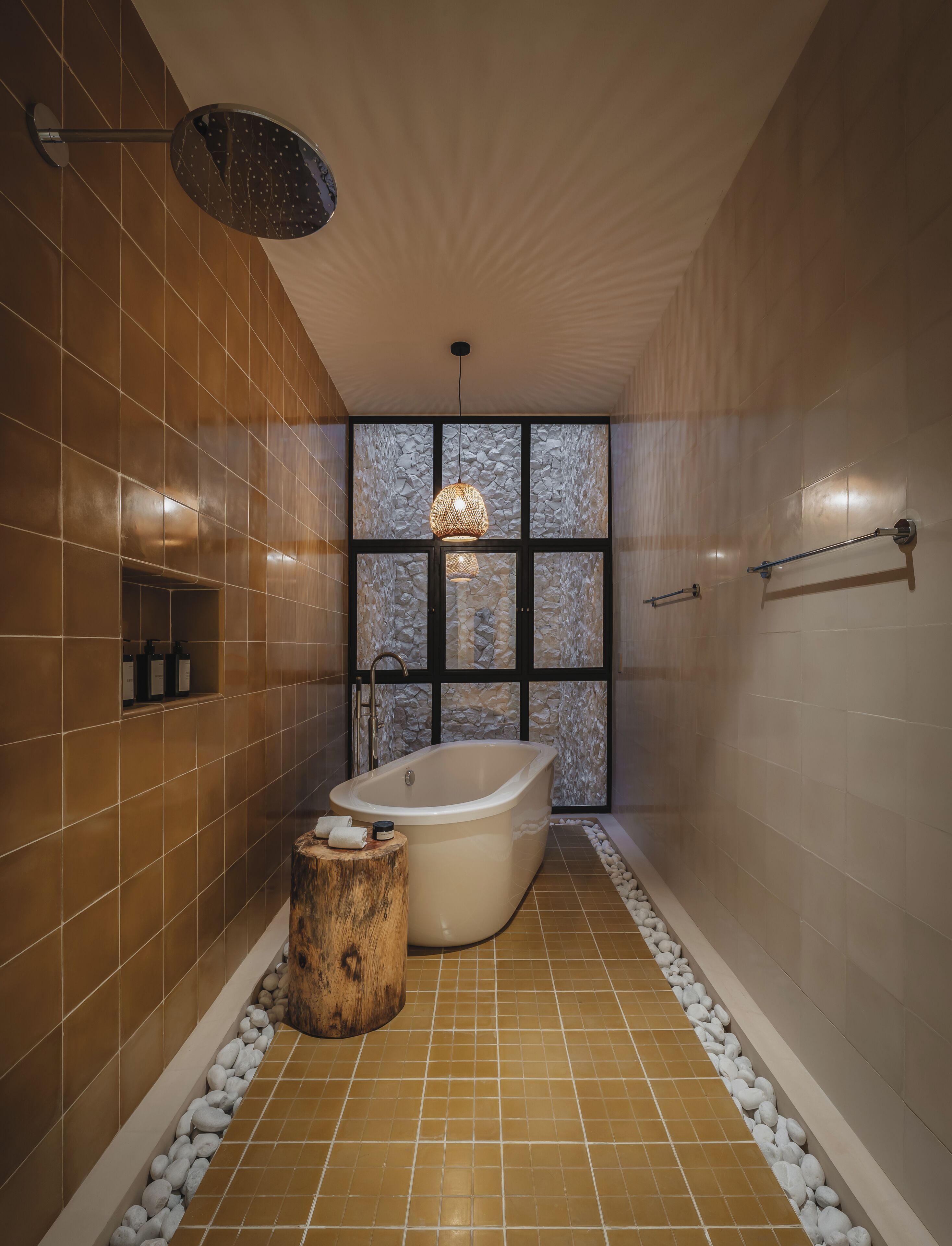 A modern bathroom with a freestanding bathtub, a stone wall feature, and a wooden stool.