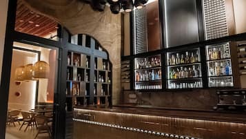 Zona de bar con mostrador de madera, estantes con botellas e iluminación circular en el techo.