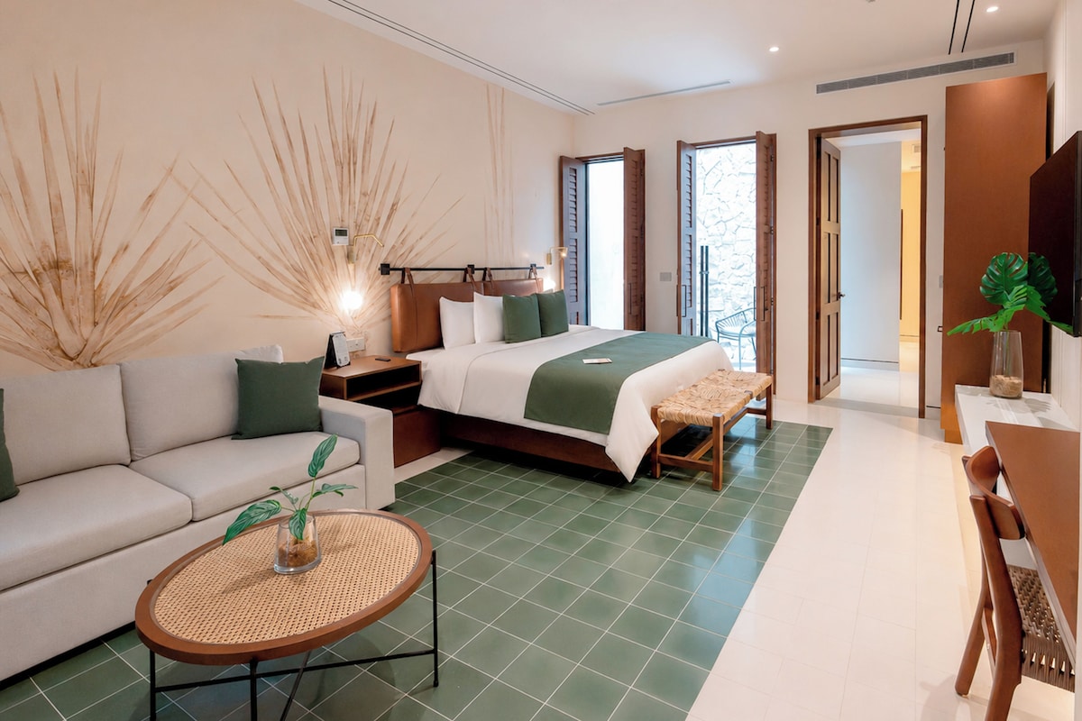 A modern hotel room with a bed, sofa, and a small table with a plant.