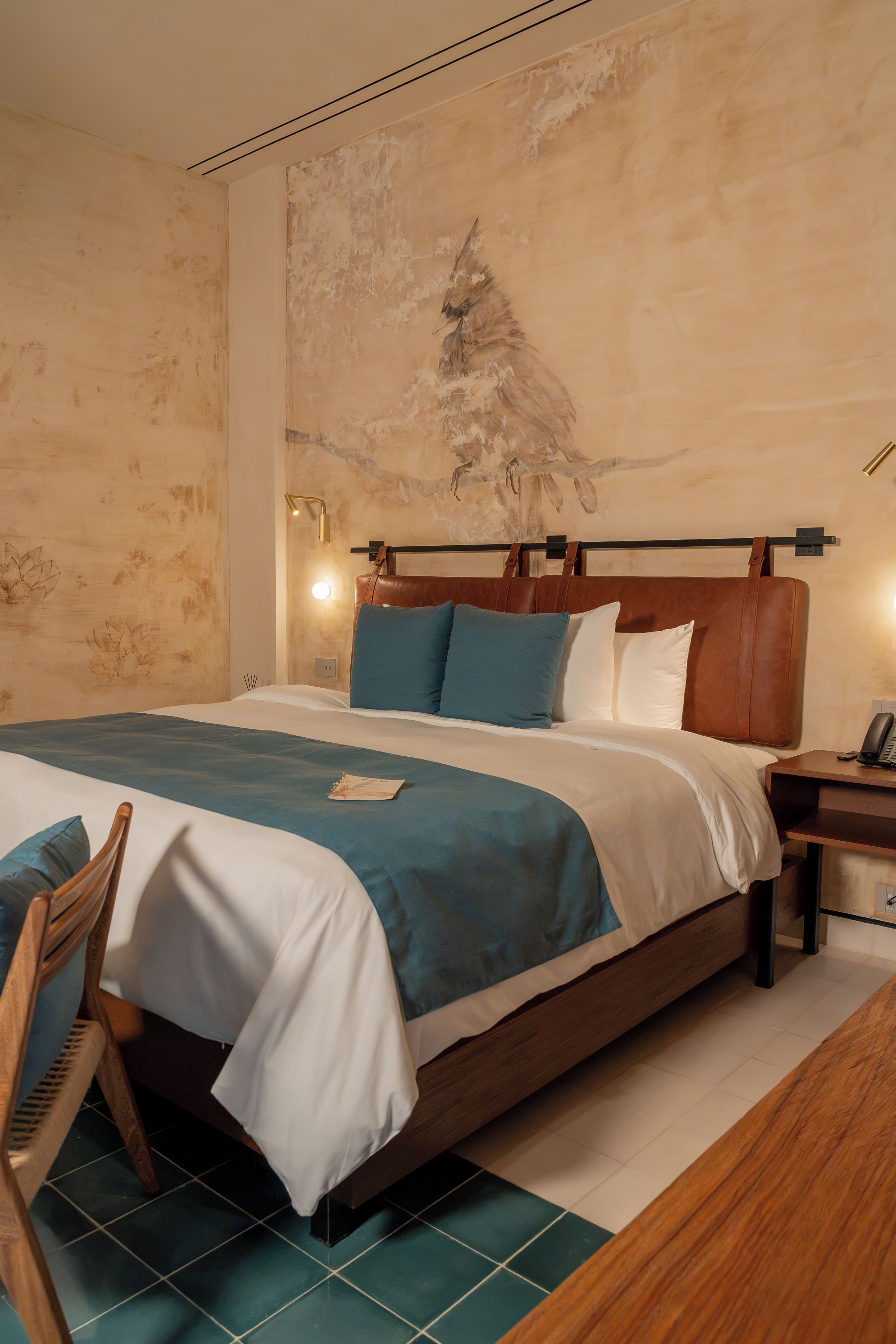 A hotel room with a large bed, a wooden headboard, a nightstand with a lamp, and a chair.