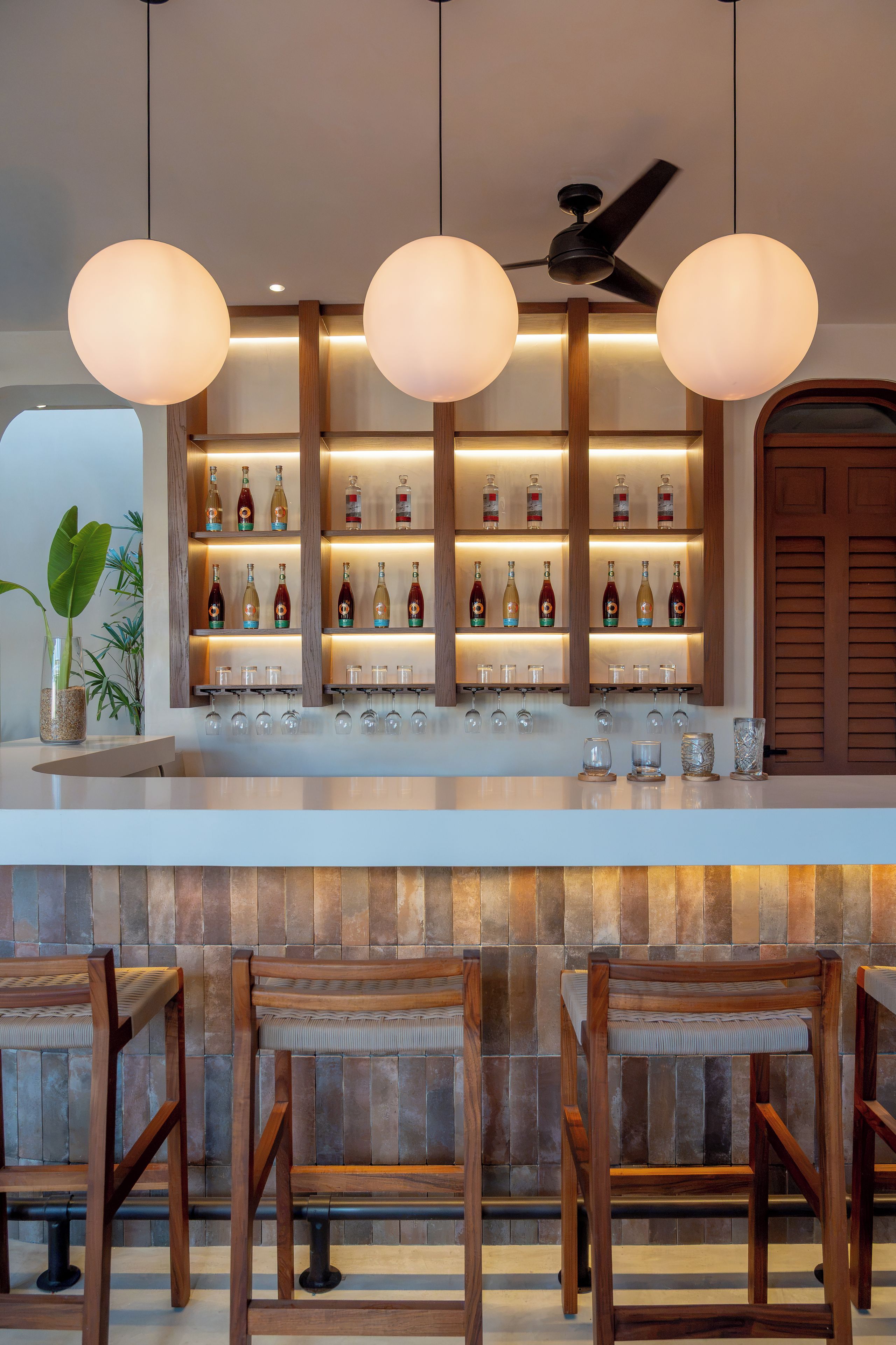 Uma área de bar com balcão de madeira, prateleiras com garrafas e copos pendurados.
