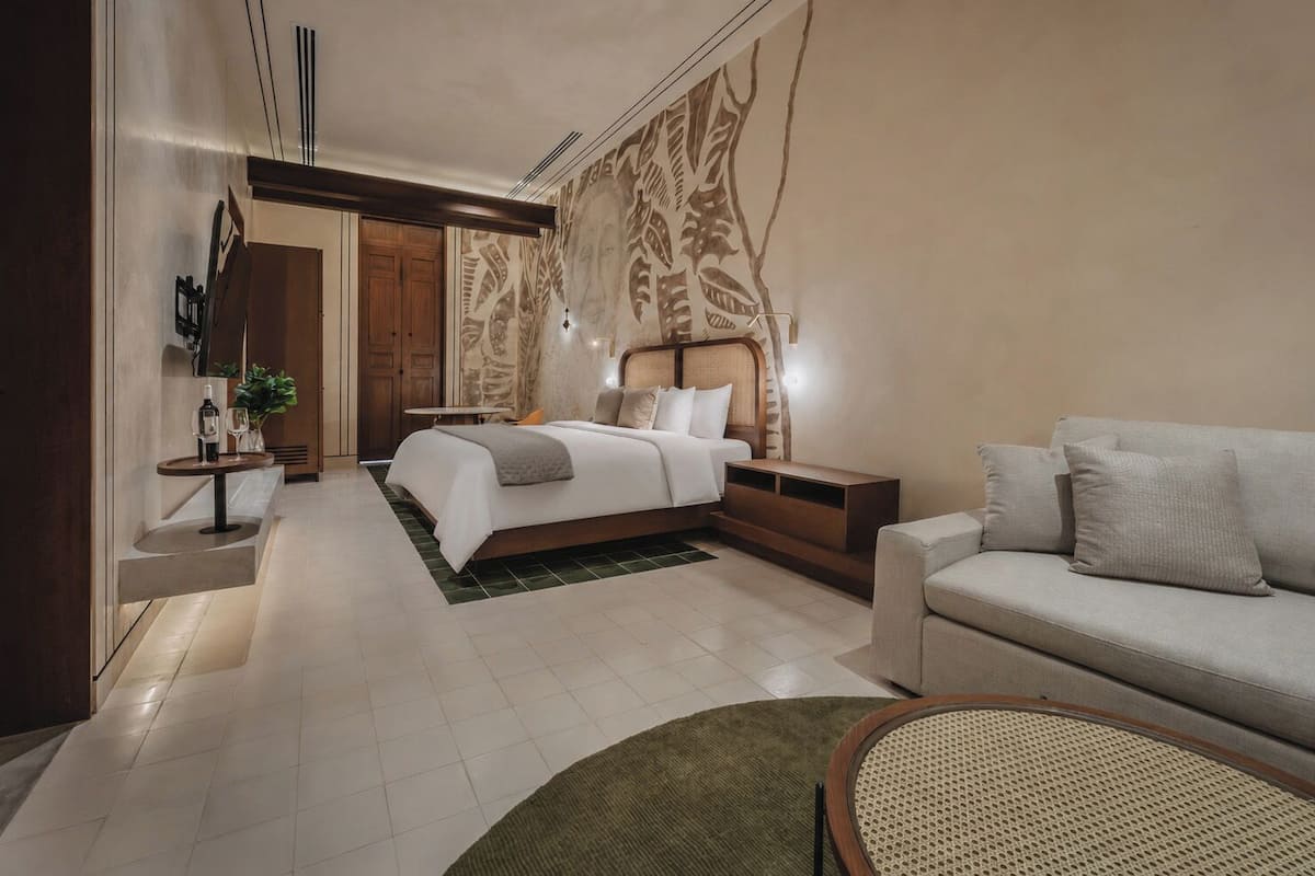 A modern hotel room with a bed, a sofa, a small table, and a wall with a leaf pattern.