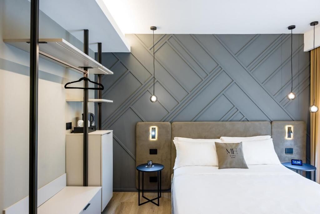 A modern hotel room with a bed, bedside tables, a wardrobe, and a hanging rack.