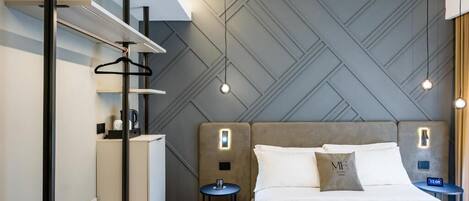 A modern hotel room with a bed, bedside tables, a wardrobe, and a hanging rack.