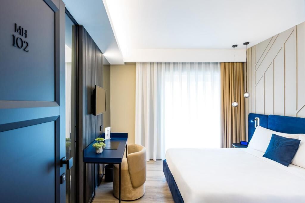 A modern hotel room with a bed, a desk, and a TV.