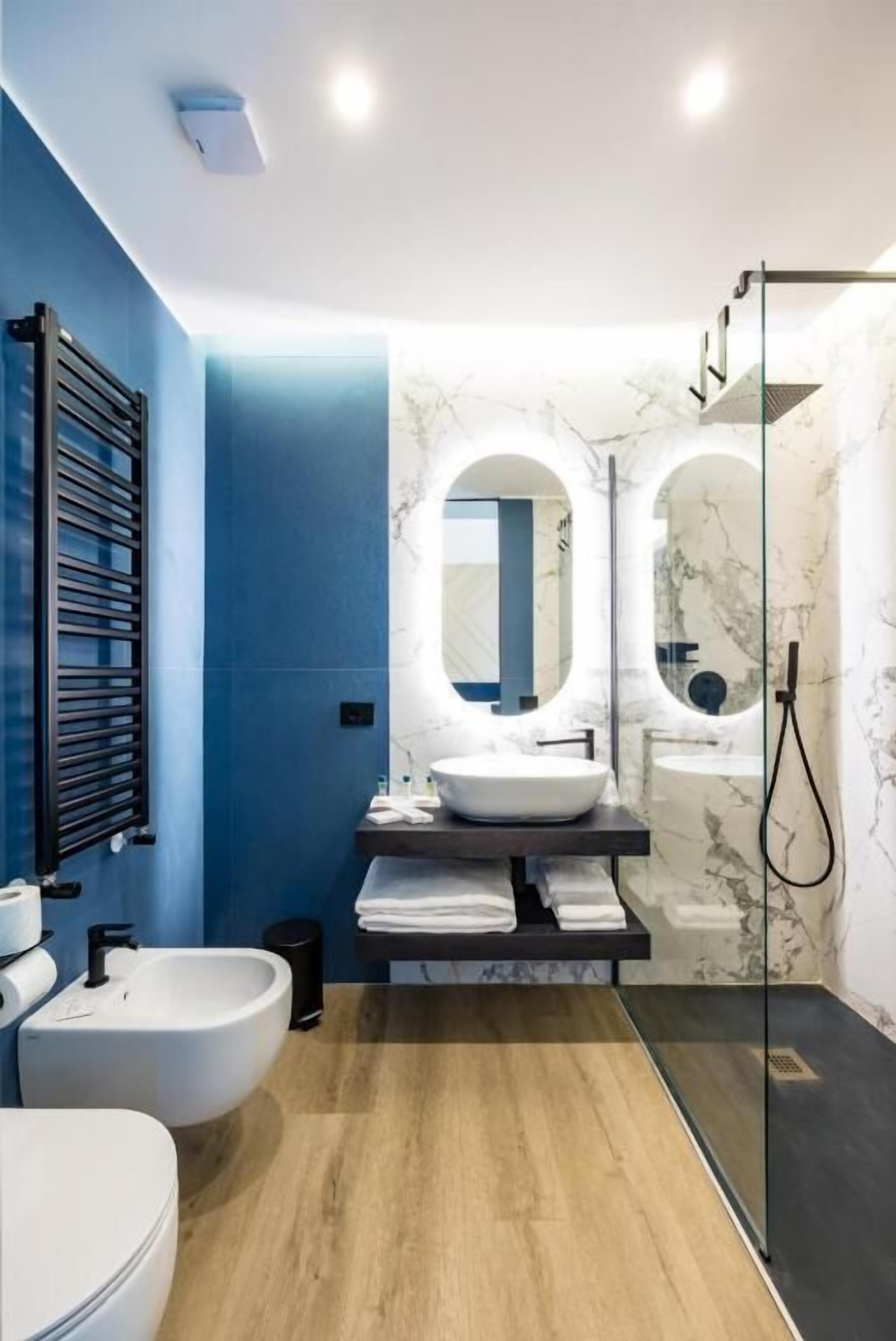 Un bagno moderno con una parete azzurra, un lavandino bianco, un bidet e una cabina doccia in vetro.