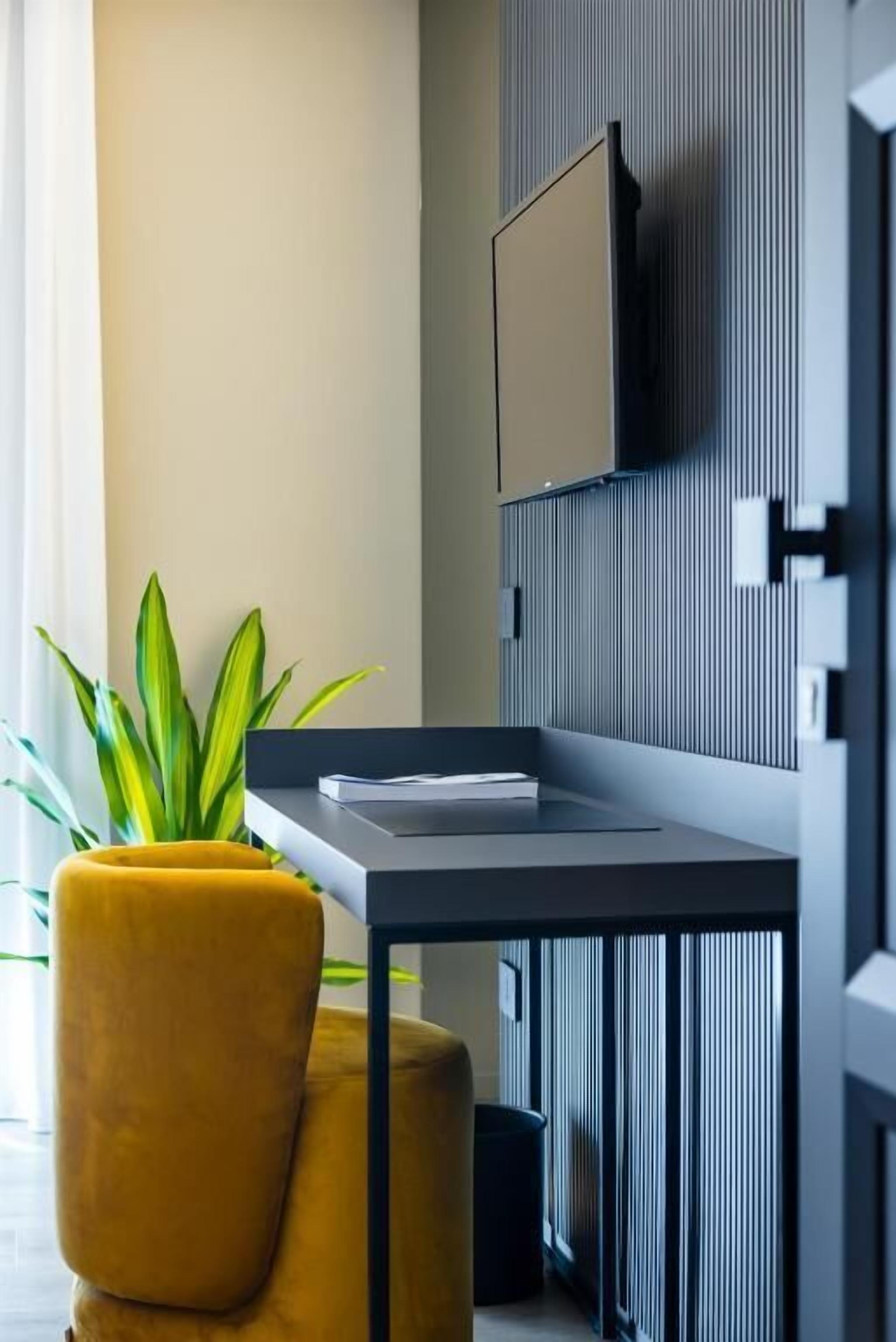 Una habitación moderna con escritorio, una silla amarilla, una planta en maceta y un televisor fijado a la pared.