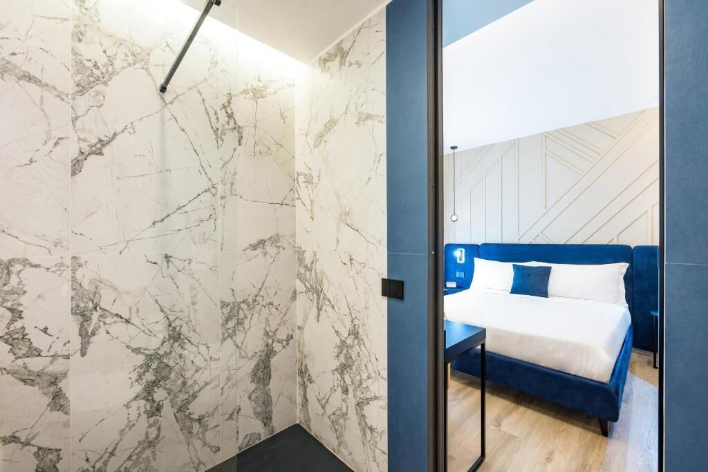 Una habitación de hotel moderna con una pared de diseño de mármol, una cama azul con ropa de cama blanca y piso de madera.