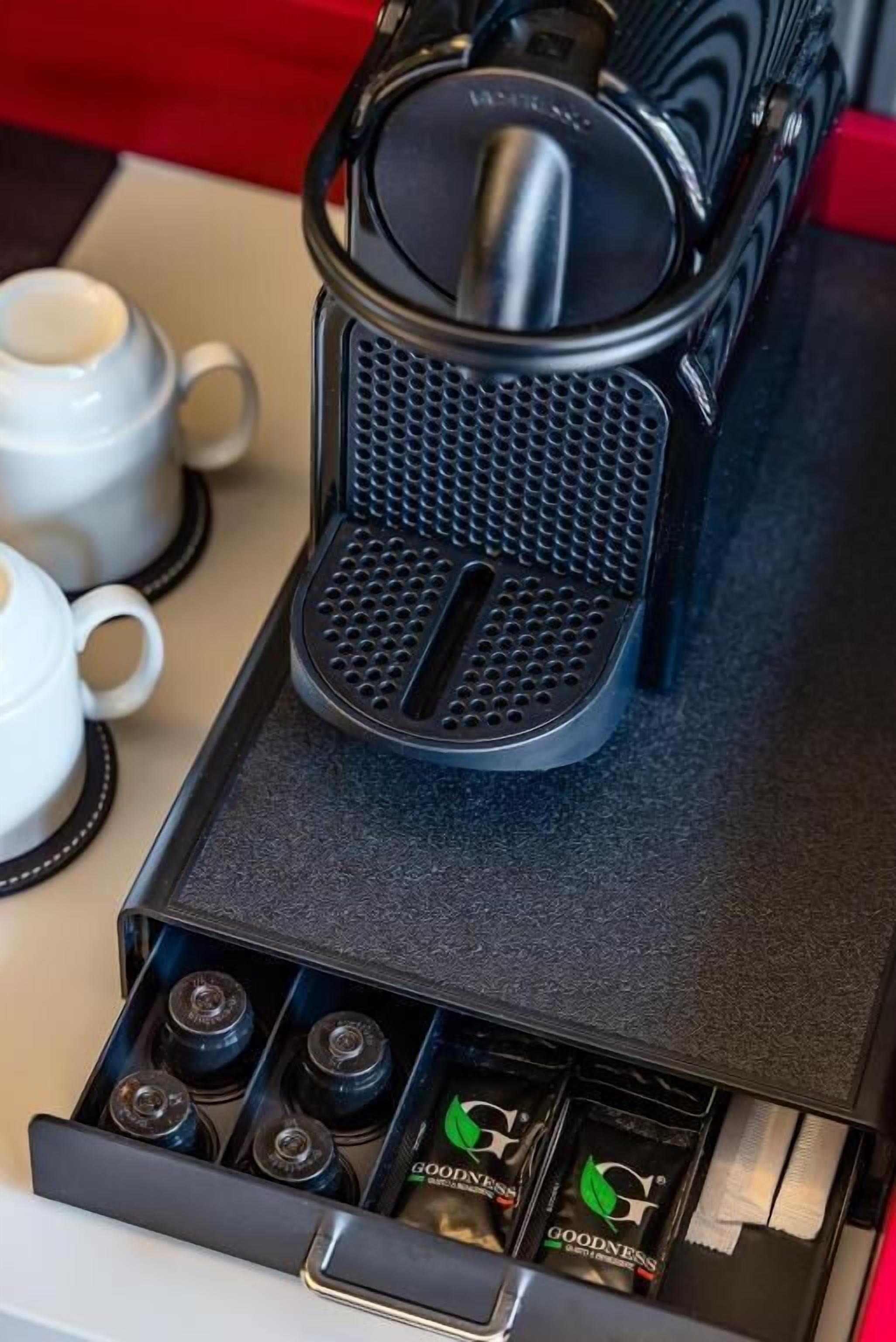 A coffee machine with a black base and a mesh filter, placed on a tray.