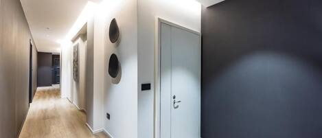 A modern hallway with a light wooden floor, a dark wall on the right, and a light-colored door with a handle.