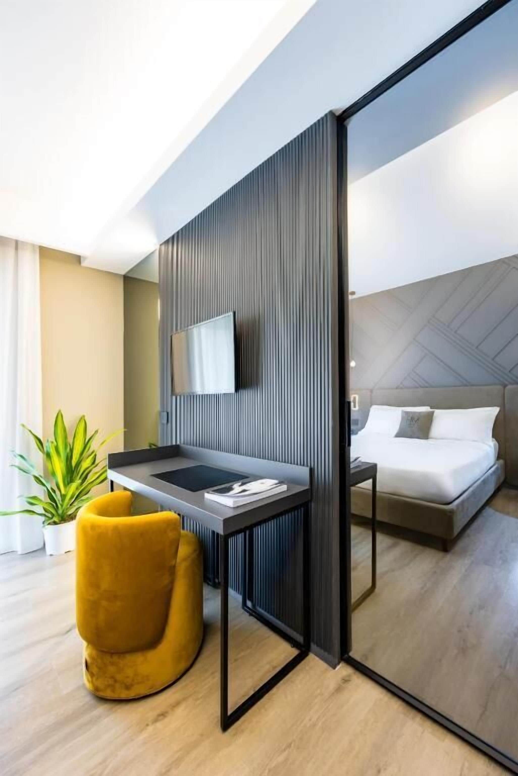Een moderne hotelkamer met een bed, een bureau, een stoel, een televisie en een plant.
