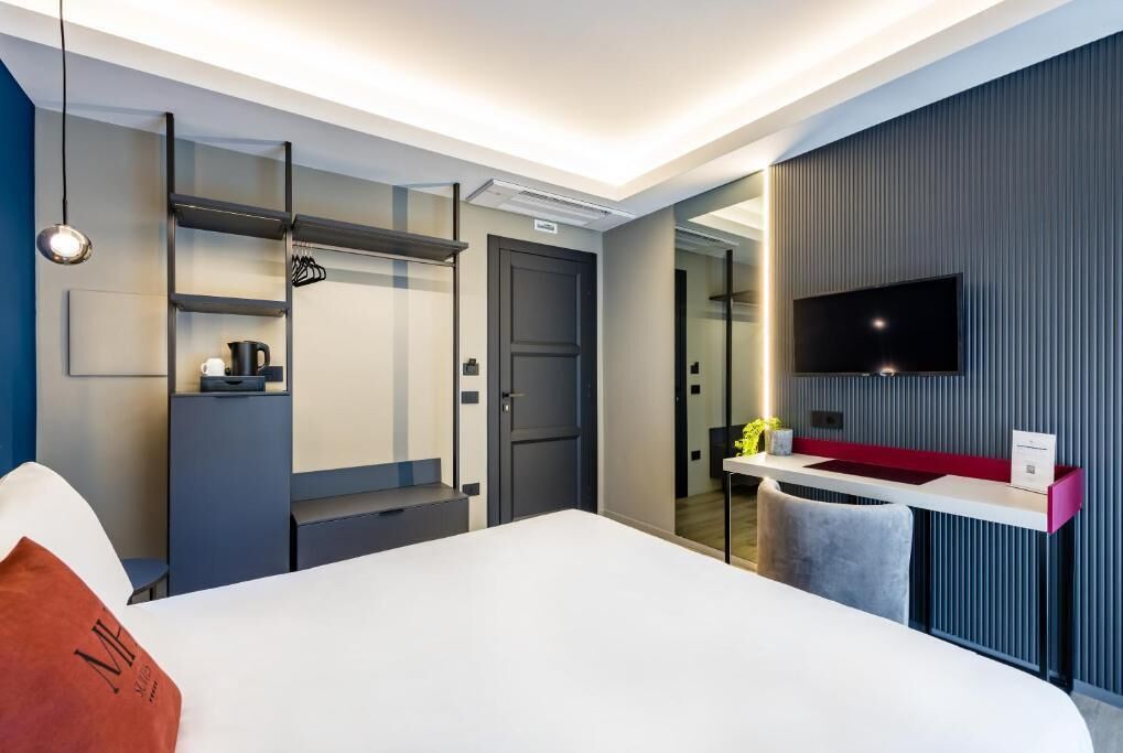 Una habitación de hotel moderna con una cama, un escritorio, un televisor y un espejo.