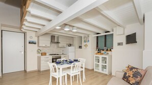 Una cucina moderna con mobili bianchi, un'area pranzo con tavolo e sedie bianche e un soggiorno con divano e TV.