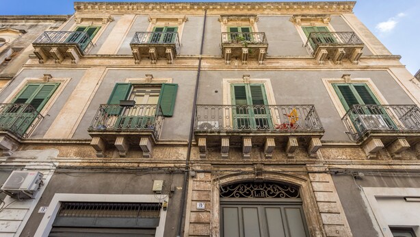 Un edificio con diversi balconi, persiane verdi e un ampio ingresso ad arco.
