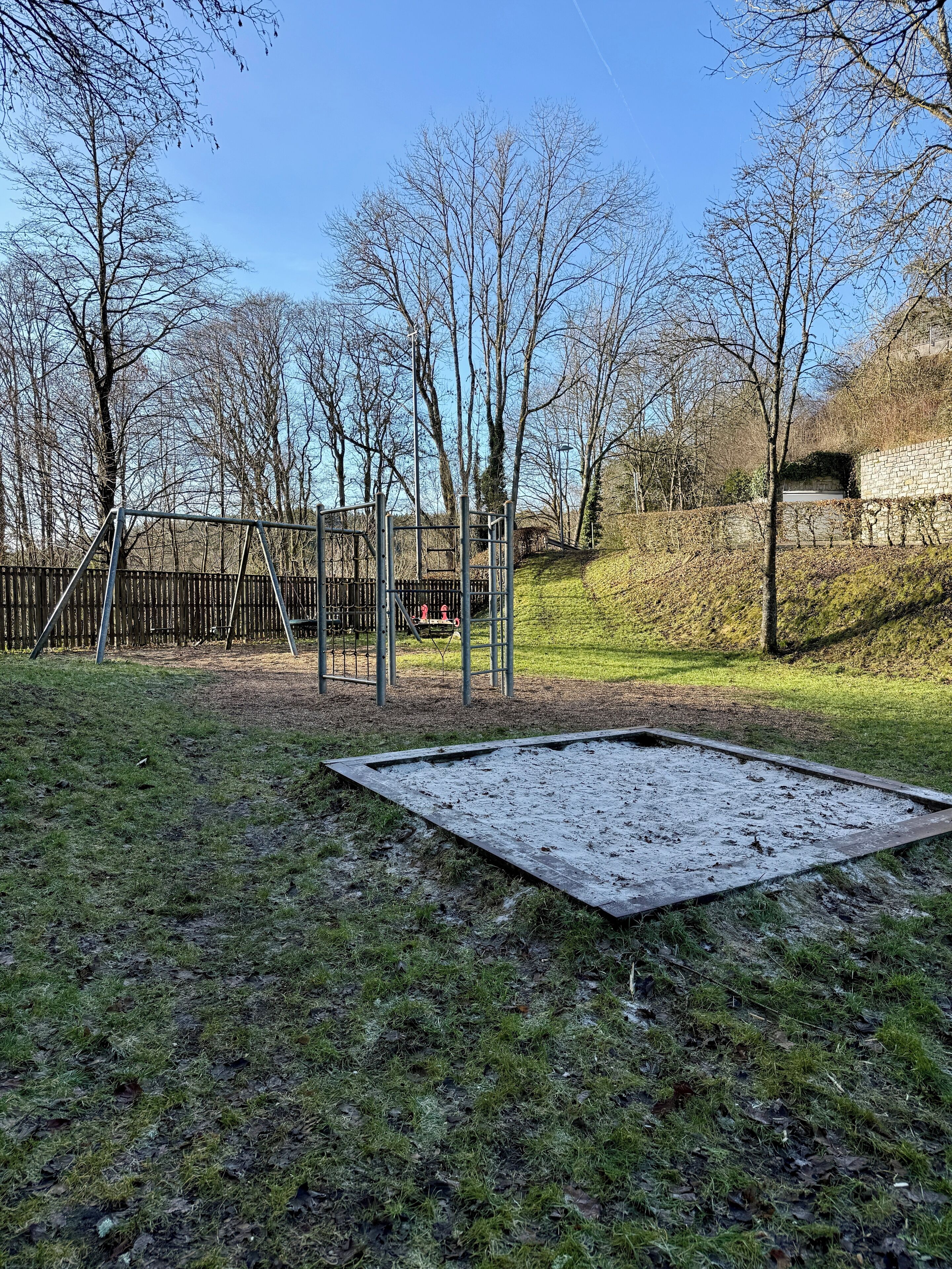 Een speeltuin met een metalen frame en schommels, omgeven door bomen en een gazon.