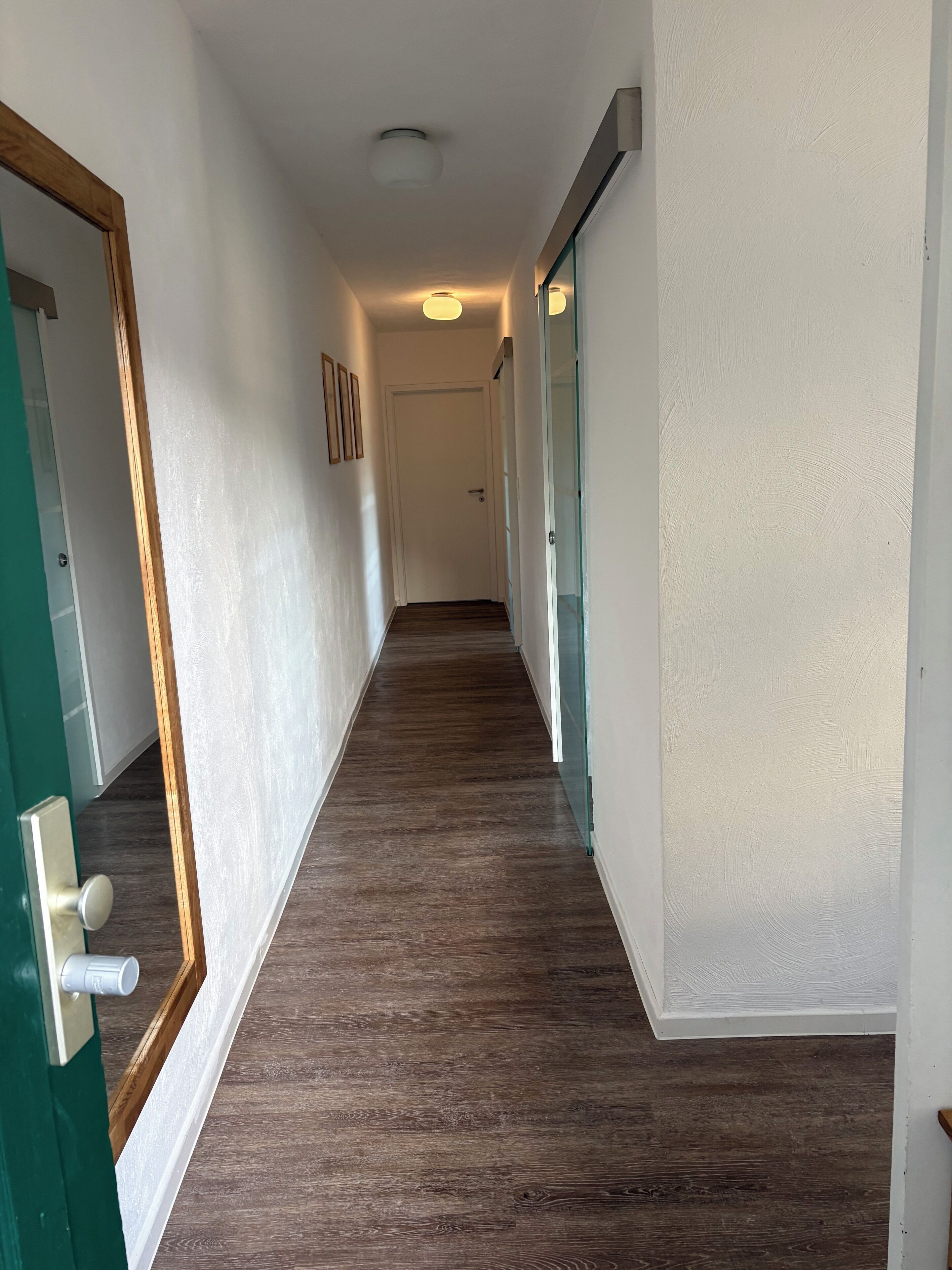 A hallway with wooden flooring, white walls, and a green door frame.