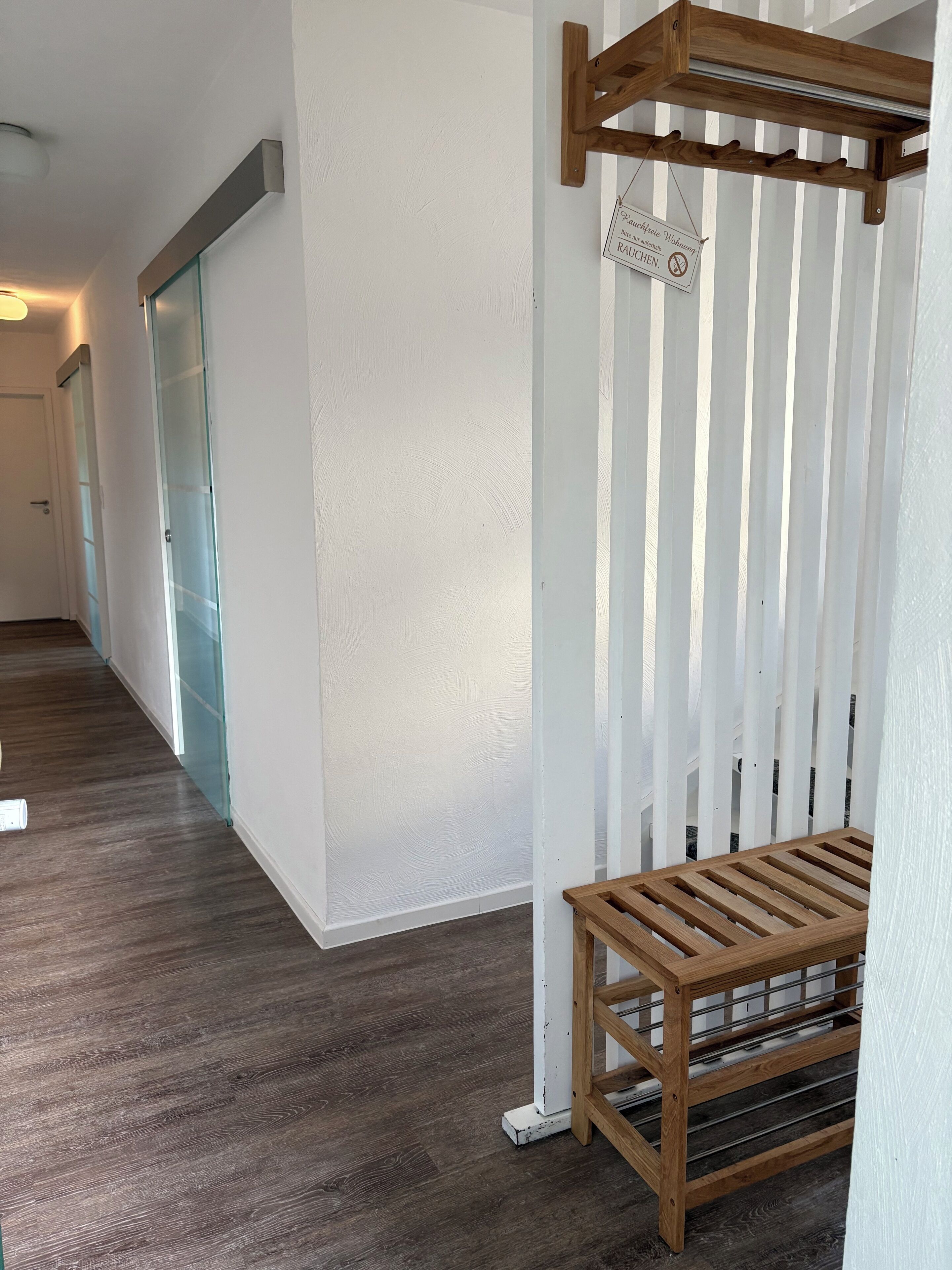 A hallway with a wooden bench, a glass door, and a sign on the wall.