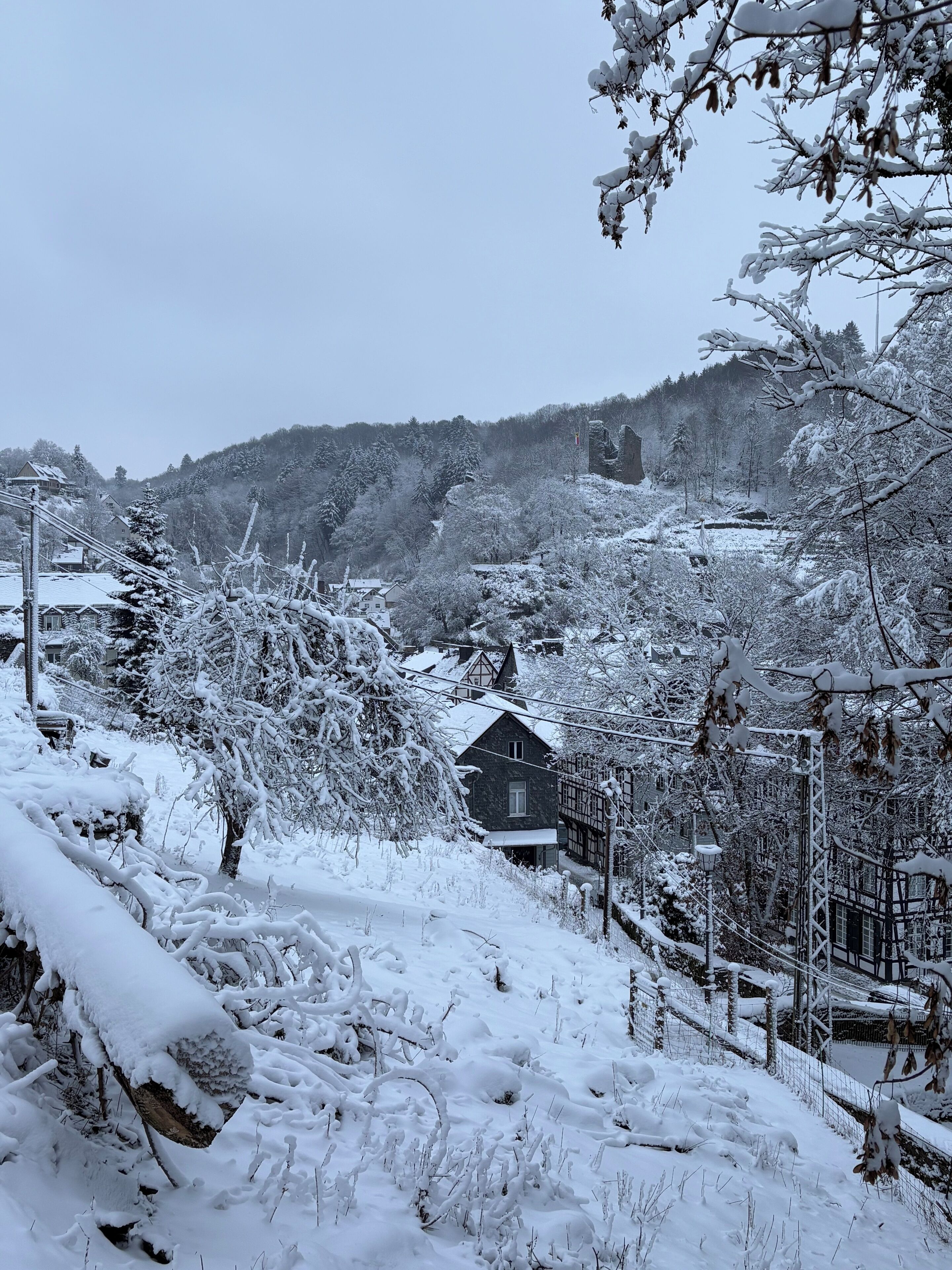 Ein verschneites Dorf mit traditionellen Häusern, einem Holzzaun und einer Hügelkette im Hintergrund.