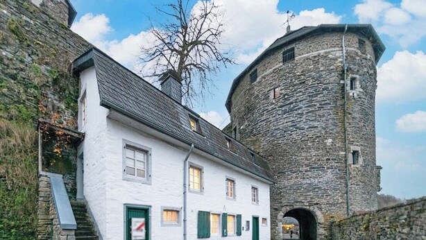 Une tour de pierre et un bâtiment blanc avec un escalier et des volets verts.