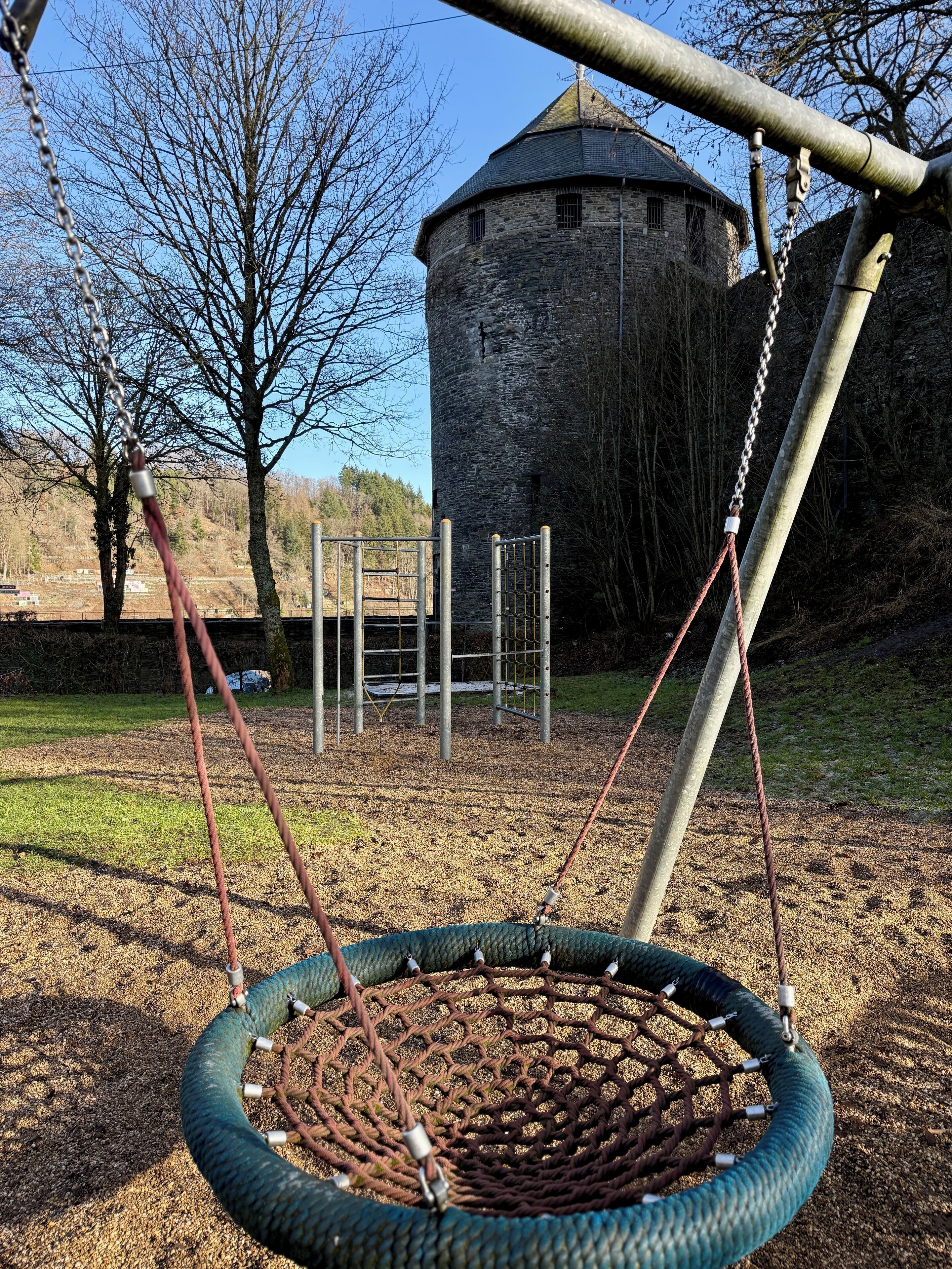 Un columpio con neumático, una cerca de metal y una torre de piedra al fondo.