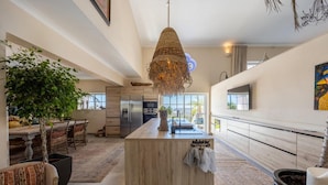 A spacious kitchen with a central island, a dining area with chairs, a large potted plant, and a hanging light fixture. - Bedroom in a Villa, Budens (Vila do Bispo)