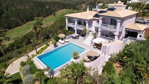 A large, two-story house with a swimming pool, surrounded by lush greenery and a hilly landscape. - Bedroom in a Villa, Budens (Vila do Bispo)